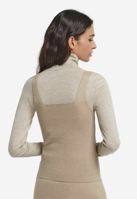 Beżowy dzianinowy top bez rękawów z kwadratowym dekoltem, nałożony na jasnobeżowy golf. Miękka faktura, dopasowany krój, gładka tkanina.