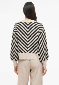 Pull rayé beige et noir avec un motif en zigzag, doté d'une texture côtelée et de manches ballon, fini par un ourlet court.