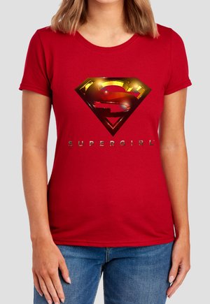 Woman wearing a red t-shirt with a shiny gold and red Supergirl emblem and the word "SUPERGIRL" below it.