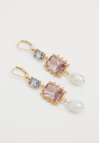 Χρυσά κρεμαστά σκουλαρίκια με κομμάτι φωτεινού ροζ και μπλε τετραγωνικού πολύτιμου λίθου, με μια πέρλα στην κάτω πλευρά, τοποθετημένα σε διακοσμητικό πλαίσιο.