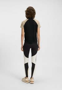 Snygg träningsoverdel i svart med beige accenter, tillsammans med high-waisted leggings som har svarta och krämfärgade paneler samt beige detaljer.