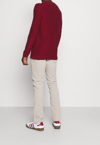 Långärmad vinröd stickad topp, beige byxor och vita sneakers med röda ränder. Toppen har en rund halsringning och avslappnad passform.