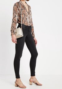 Chemise à manches longues avec un imprimé serpent brun et noir, associée à un jean noir taille haute et des sandales à talons carrés beige. Petit sac bandoulière.