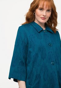 Turquoise bloemenpatroon jasje met kraag, drie knopen en zijzakken; gemaakt van gestructureerde stof, mouwen tot de elleboog.