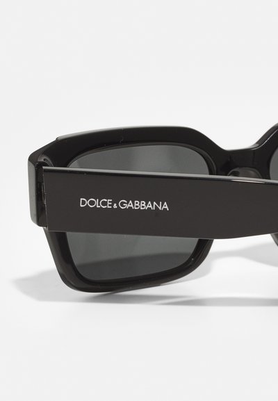 Ochelari de soare negri cu un design unghiular, având lentile întunecate și un cadru îndrăzneț. Logo-ul "DOLCE & GABBANA" în culoare albă pe braț.