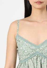 Grønn blomstermønstrete kjole med blonde detaljer, justerbare tynne stropper og en tettsittende overdel som glir over i en samlet skjørt.