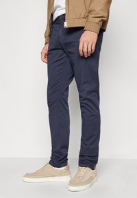 Chinos slim-fit di colore blu navy realizzati in misto cotone, con passanti per cintura e tasche frontali; indossati con sneakers beige.