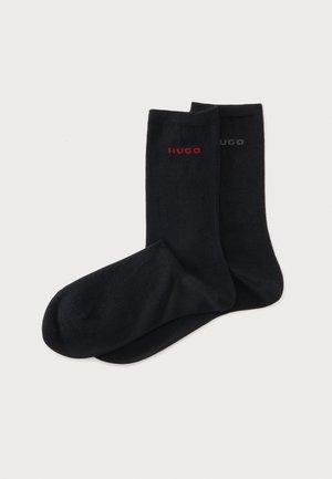 Paire de chaussettes noires montant jusqu'au milieu du mollet avec le logo "HUGO", l'une rouge et l'autre gris foncé, sur un fond uni clair.
