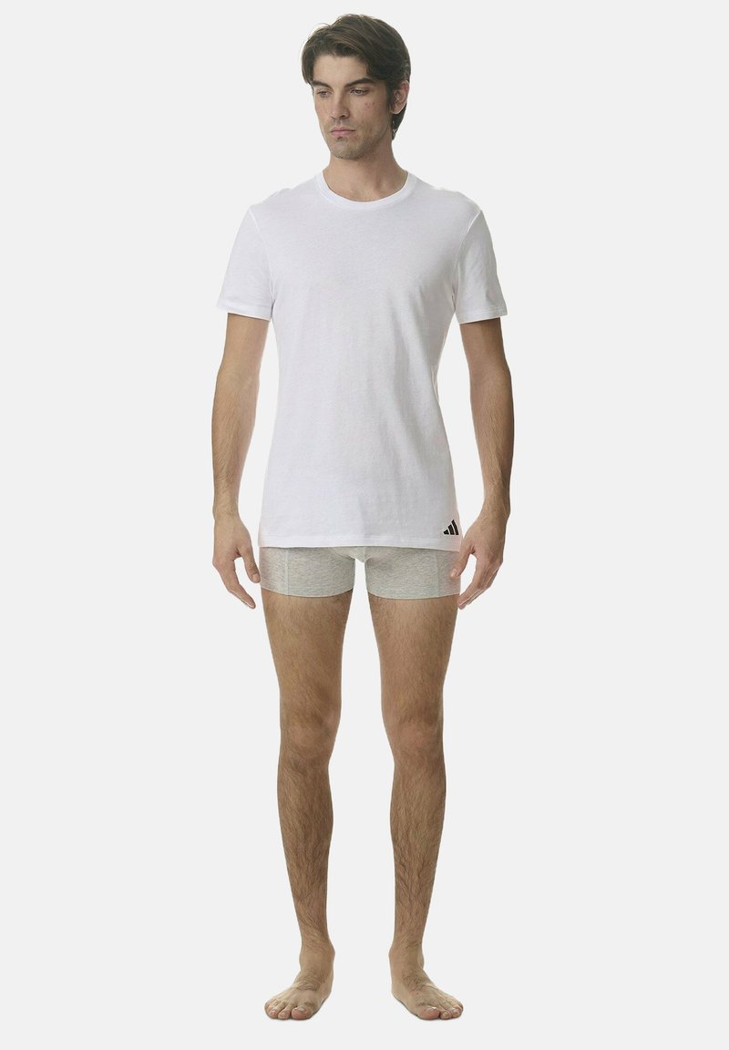 Biała bawełniana koszulka w połączeniu z jasnoszarymi bokserkami. Model stoi boso, prezentując prosty i funkcjonalny design bez wzorów.