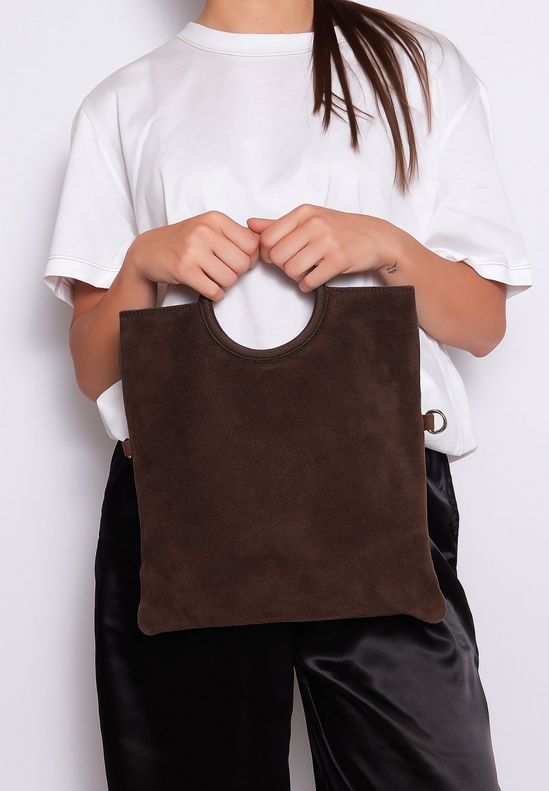 Sac fourre-tout en suède marron avec une poignée supérieure arrondie et un design minimaliste. La texture paraît douce et sans ornement.