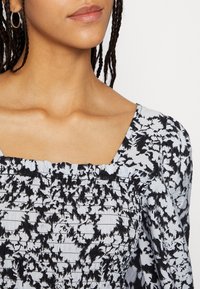 Top smock em padrão preto e branco com decote quadrado e mangas bufantes, confeccionado em tecido leve.