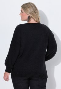 Svart tröja med avslappnad passform, batwing-ärmar, texturerad stickning och ribbade mudd. Bärs med mörka jeans, sedd bakifrån.