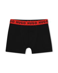 Μαύρα μποξεράκια ανδρών με φαρδύ κόκκινο μπάντα μέσης που φέρει επαναλαμβανόμενο κείμενο "HUGO" σε μαύρα γράμματα.