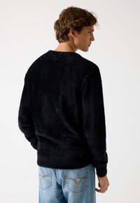 Zwarte, donzige trui met ronde hals en lange mouwen, gecombineerd met lichtblauwe jeans met een opvallend zakontwerp.