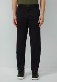 Schwarze Baumwollhose mit geradem Schnitt, Knopfverschluss vorne, Gürtelschlaufen und Seitentaschen, kombiniert mit schwarzen Sneakers und einem grünen Hemd.