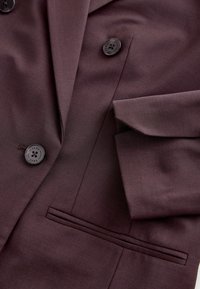 Tamno maroon sako s glatkom teksturom, dvostrukim kopčanjem, dva crna dugmeta i elegantnom detaljnom džepu na donjoj lijevoj strani.