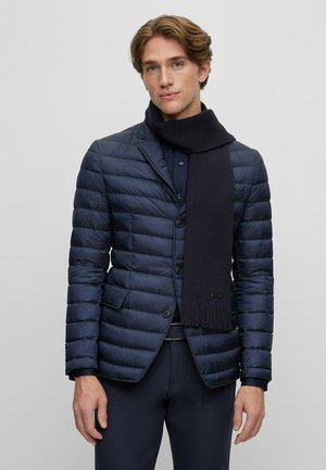 Navy puffer jacket with a quilted design, single-breasted buttons, and side pockets. Paired with a dark knitted scarf.