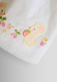 Tissu blanc présentant des motifs de souris brodés avec des couleurs pastel douces, des fleurs, et des détails incluant une fraise dans la main de la souris.