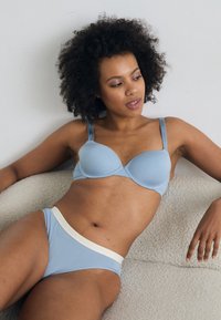 Lys blå polstret BH med justerbare stropper og matchende bikinitruser med kontrasterende hvit kant. Glatt stoff og tettsittende design.