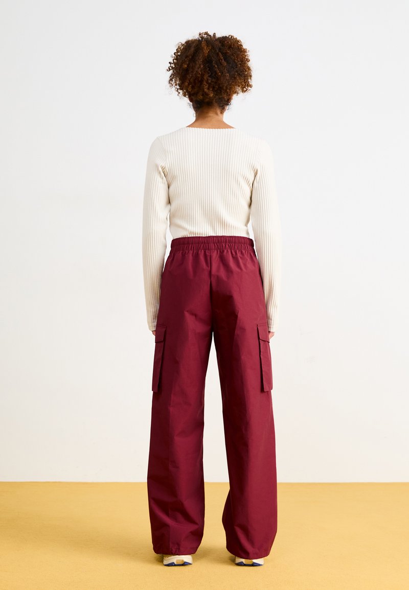 Pantalones cargo burdeos con cinturilla elástica, que cuentan con dos bolsillos laterales y un corte relajado, combinados con una camiseta de manga larga de canalé en color crema.