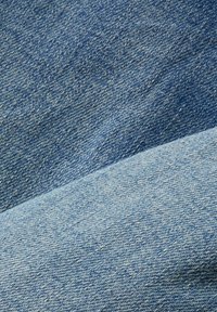 Texture de tissu en denim bleu montrant deux pièces qui se chevauchent avec des nuances distinctes et des motifs de fils tissés.