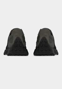 Οπίσθια όψη ενός ζευγαριού σκούρων πράσινων και μαύρων αθλητικών παπουτσιών με υφασμένους λαστιχένιους πάτους και πάνελ τακουνιού από σουέντ σε γκρι φόντο.