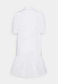 Robe-chemise blanche à manches courtes avec col, poignets boutonnés et un ourlet volanté froncé, vue de dos sur un fond uni.