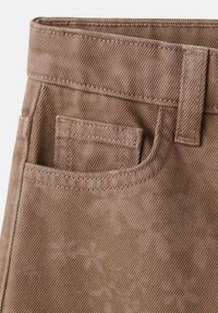Pantaloni in twill marrone con superficie strutturata, dotati di passante per cintura e una tasca posteriore singola. Dettagli cuciti evidenziano il design.