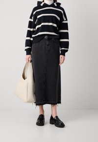 Sudadera con capucha azul marino a rayas con detalles en caqui, falda vaquera larga negra con dobladillo deshilachado, bolso tote beige y mocasines plataforma negros.