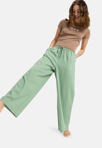 Lichtbruine t-shirt met korte mouwen met witte grafische opdruk, gecombineerd met losse, mintgroene broek met wijde pijpen, voorzien van een elastische tailleband en trekkoord.