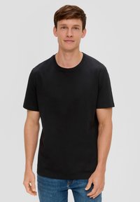 T-shirt en coton noir avec un col rond et des manches courtes, porté par une personne en jean bleu sur un fond uni.