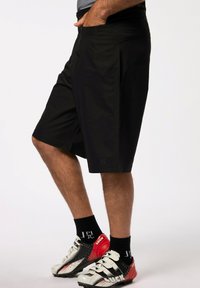 Sorte atletiske shorts med løs pasform, der har lommer, en glat tekstur og design til knæet. Bæret sammen med røde og hvide fodboldstøvler.