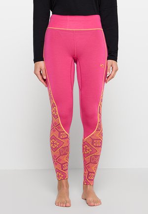 Frau trägt leuchtend pinke Leggings mit orangefarbenen geometrischen Mustern an den unteren Beinen und orangen Nahtdetails, kombiniert mit einem schwarzen Langarmshirt.