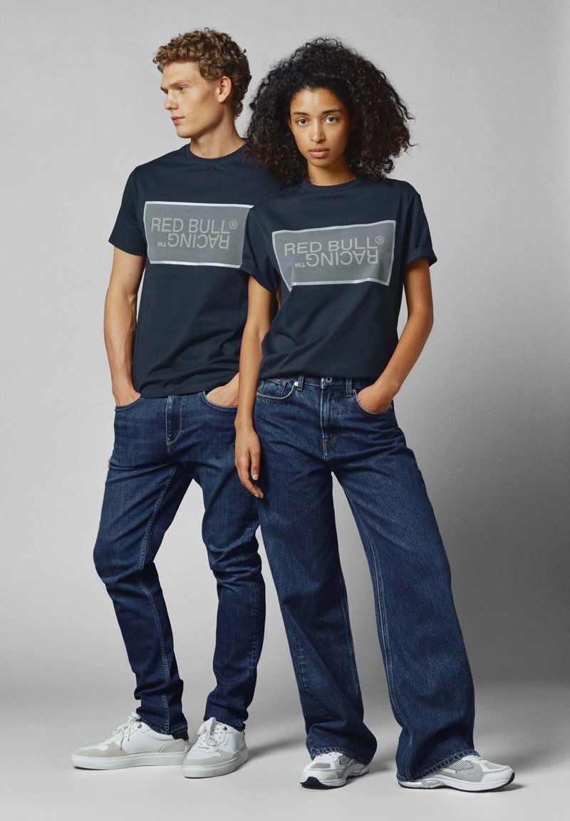 Marineblauwe T-shirts met een grijze "RED BULL RACING" logo. Gecombineerd met donkerblauwe jeans en witte sneakers. Casual pasvorm, korte mouwen en eenvoudig ontwerp.
