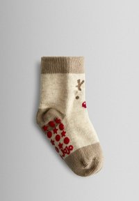 Calcetines de punto con un patrón a rayas en beige y crema, puño marrón y puntos y estrellas rojas en la suela para mayor agarre.