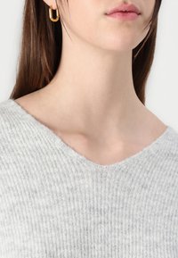 Light gray ribbed sweater featuring a V-neck design and soft texture. Gold hoop earring accentuating the model's neck and chin.