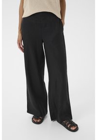 Zwarte linnen broek met wijde pijpen en een gladde textuur, voorzien van zijzakken en een ontspannen pasvorm, gecombineerd met zwarte gevlochten sandalen.