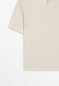 Top en maille côtelée couleur crème à manches courtes, col en V et silhouette ajustée.