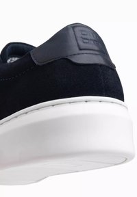 Schwarze Wildleder-Sneaker mit einer glatten Lederakzent an der Ferse, ausgestattet mit einer weißen Gummisohle und einem strukturierten Logodetail.