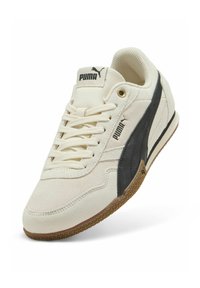 Zapatillas de ante blanco con una franja lateral negra, talón texturizado y suela de goma marrón. Diseño con cordones, con una lengua y acentos de marca.