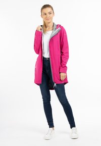 Rosa vattentät jacka med grå huva, dragkedjestängning och dragsko. Matchas med mörka jeans och vita sneakers. Slät textur.