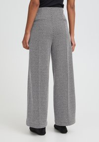 Bukser med vidde i hundetandsmønster, med høj talje, sidelommer og en struktureret sort-hvidt stof.