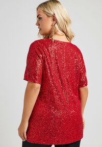 Top rojo con lentejuelas, de corte relajado, mangas cortas, escote redondo y superficie texturada. Presenta lentejuelas brillantes que producen un efecto de chispa.