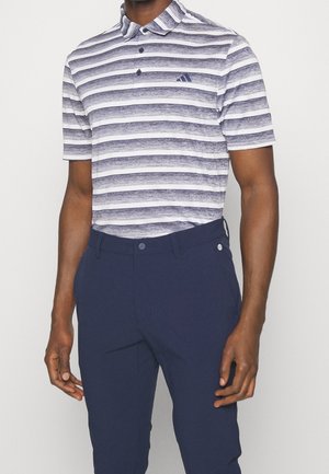 Mann trägt kurzärmeliges Poloshirt mit marineblauen und weißen horizontalen Streifen und marineblaue Hose, steht vor einem schlichten Hintergrund.