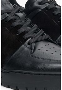 Černé tenisky se směsí kůže a sametu, perforovanou špičkou, plochými tkaničkami a texturovanou gumovou podrážkou.