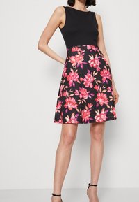 Un haut sans manches noir se transforme en une jupe florale avec des fleurs roses et orange, présentant une forme évasée en A, une texture lisse et une longueur genoux.