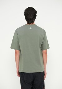 Ελαιόχρωμο βαμβακερό μπλουζάκι με στρογγυλή λαιμόκοψη και κοντά μανίκια. Διαθέτει λευκό λογότυπο Jordan στην πλάτη. Απλός, χαλαρός σχεδιασμός.