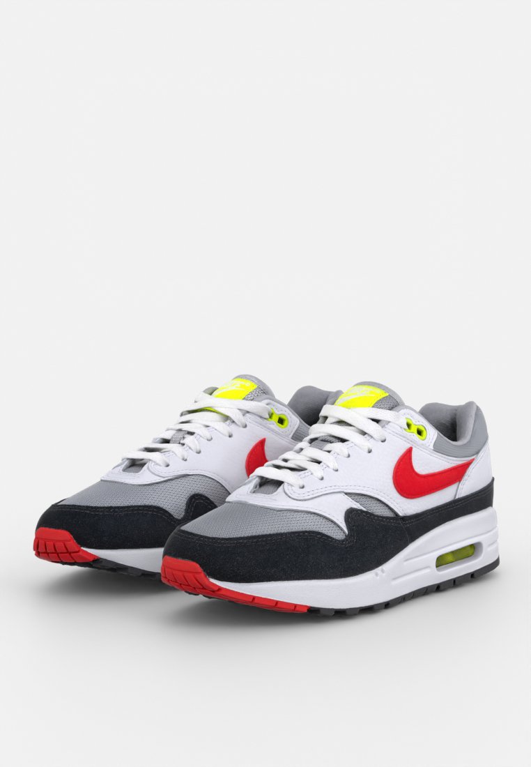 Baskets avec une tige en maille blanche, des accents en daim gris, un swoosh rouge et une semelle en caoutchouc noire dotée d'une unité Air visible et de détails en néon jaune.