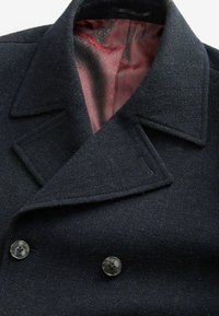 Dunkelblauer Wollmantel mit strukturiertem Kragen, doppelt knöpfbarem Verschluss und fester roter Musterfutter.