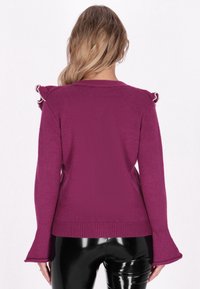 Suéter morado ajustado con un tejido texturizado, que presenta detalles con volantes en los hombros y puños acampanados. Acabado de tela suave.